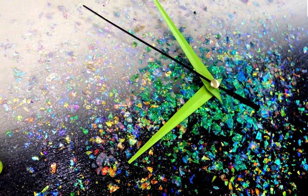 Nahaufnahme einer Uhr mit Farbverlauf und schillernden Flocken, Zeiger in Limettengrün und Schwarz.
