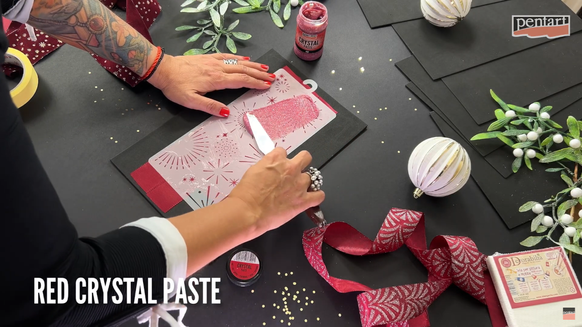 Eine Frau trägt rote Pentart Crystal Paste auf eine Schablone
